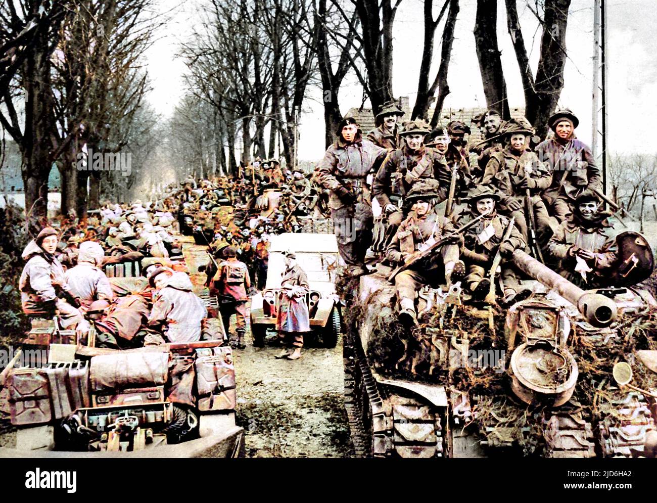 British infantry riding on Sherman tanks towards the Reichswald area, Germany, February 1945. Left of photograph, anti-tank guns and their crews can be seen. Colourised version of: 10218116       Date: 1945 Stock Photo