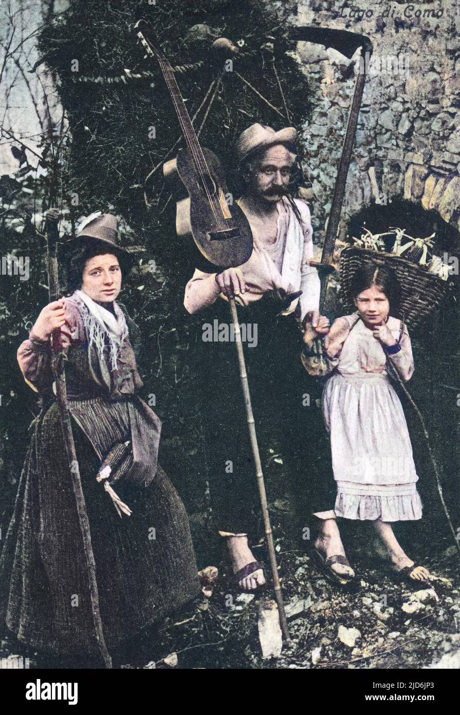 Italian/Swiss border - Ticino Family - Lake Como - A country family return from harveting heads of corn. The gentleman (centre) is balancing his guitar against a huge bundle of foliage he is carrying on his back. Colourised version of: 10651853       Date: circa 1910s Stock Photo