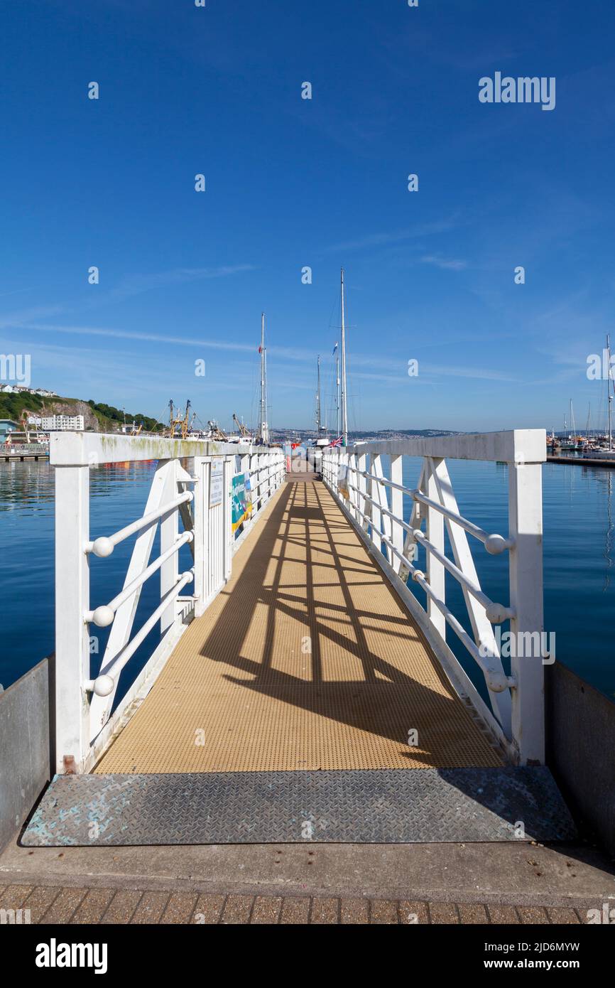 Brixham Harbour, Devon, England, UK –  a gangway with white rails set against a deep blue sky and blue sea. Wide-angled shot Stock Photo