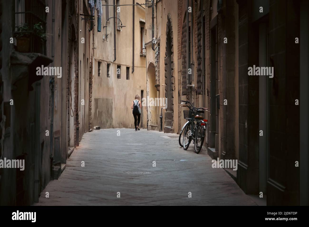 Woman walks alone in alley way in the medieval city of Lucca, Italy. Stock Photo