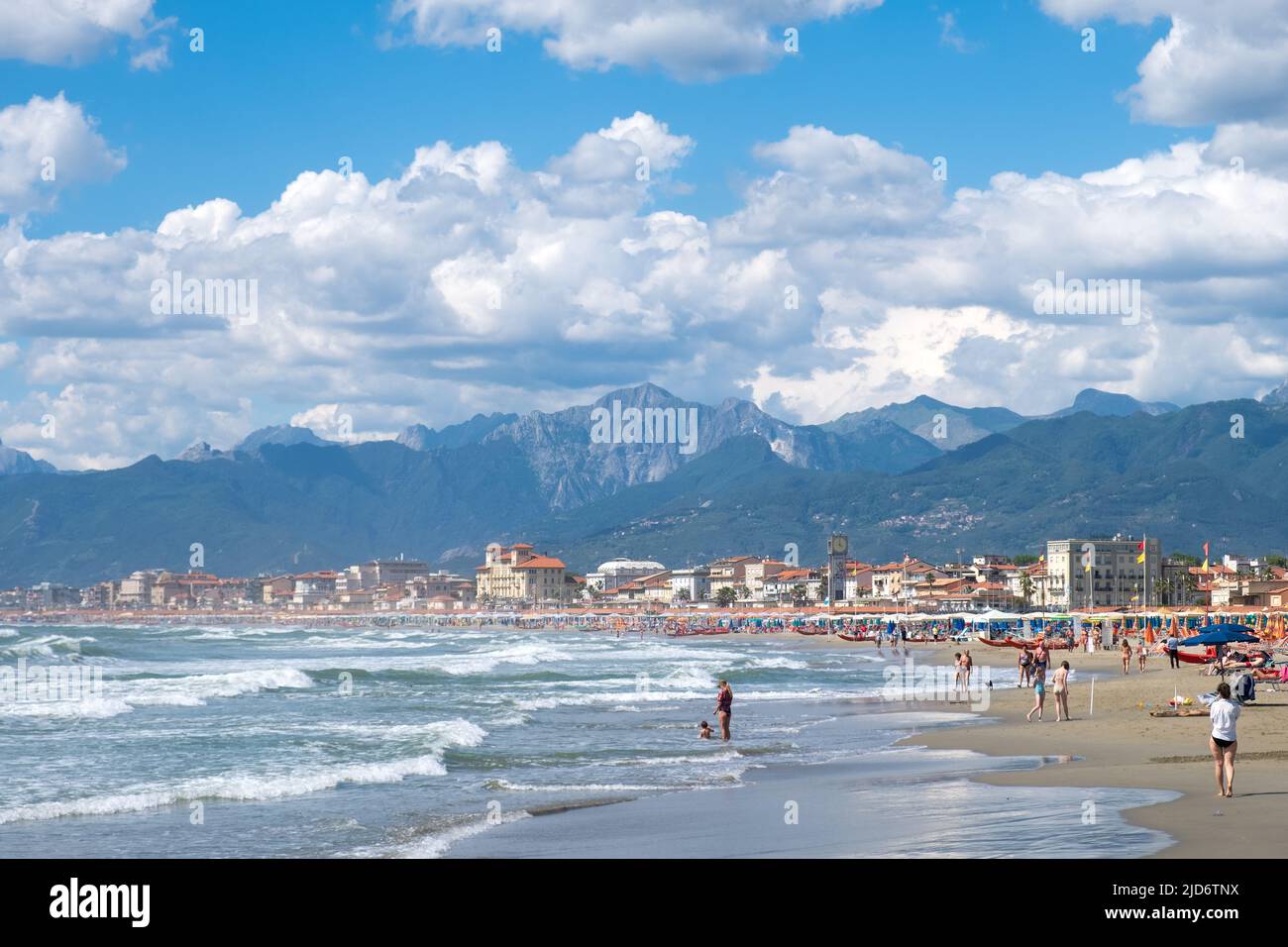 Viareggioi, Italy - June 9, 2022: Beachgoers, young and old, enjoy the surf at Viareggio, Italy. Majestic Apennine mountains and dramatic clouds frame Stock Photo