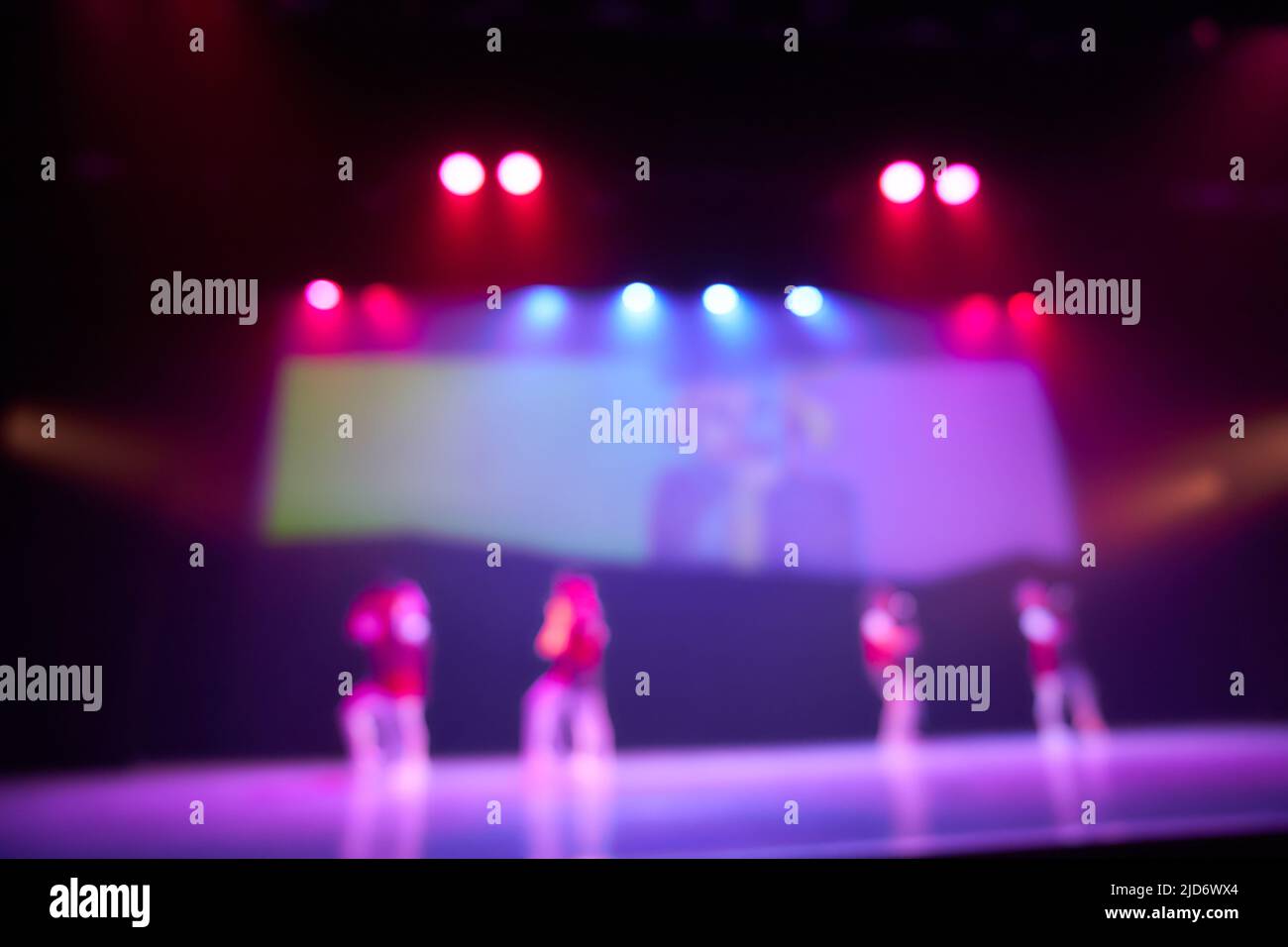 Blurred background of a dance scene with silhouettes of children dancing and a screen in the background. Bright stage lighting. Lighting devices on stage. High quality photo Stock Photo