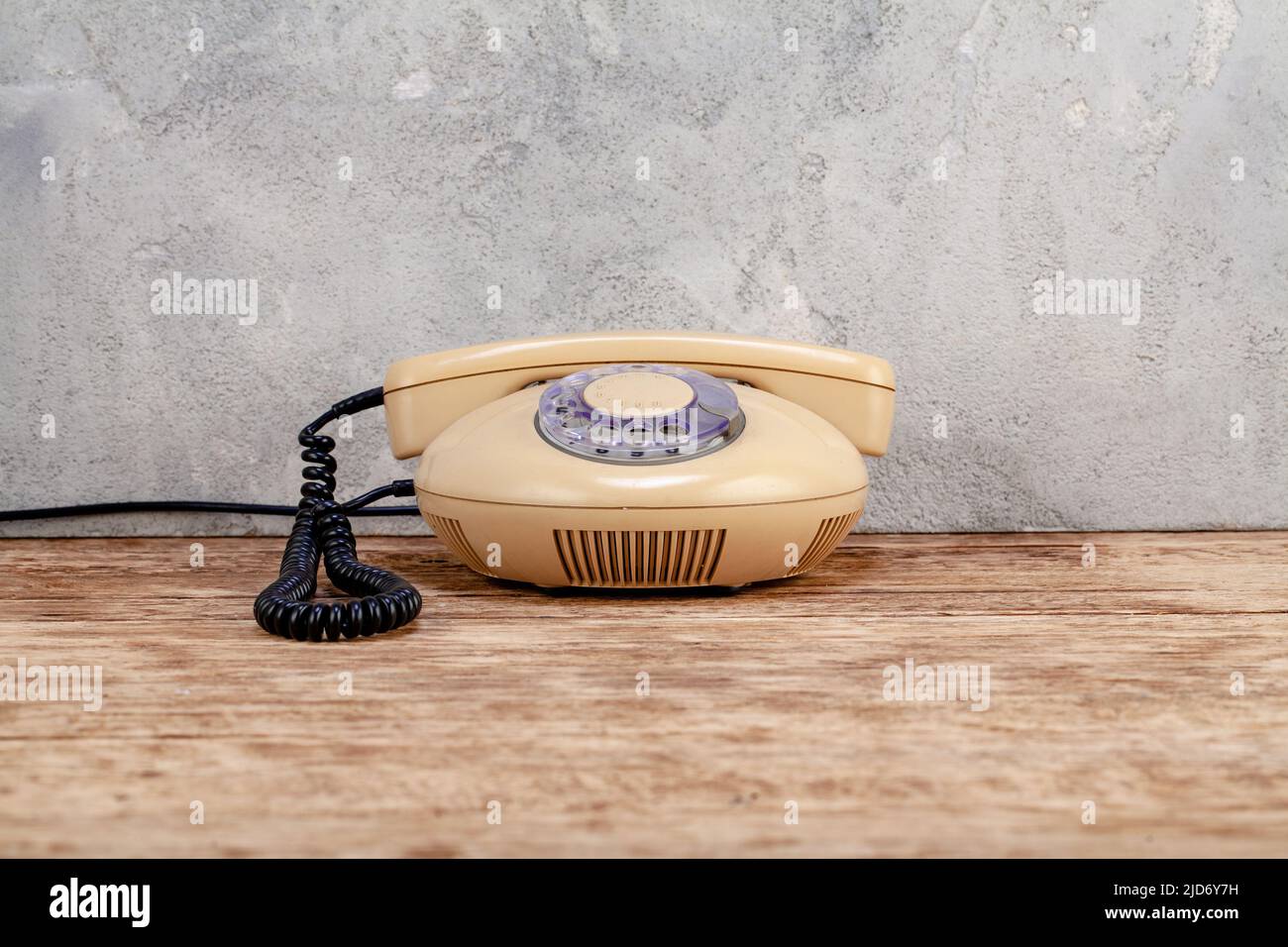 Vintage yellow rotary dial telephone on wooden table in front gray concrete background Stock Photo