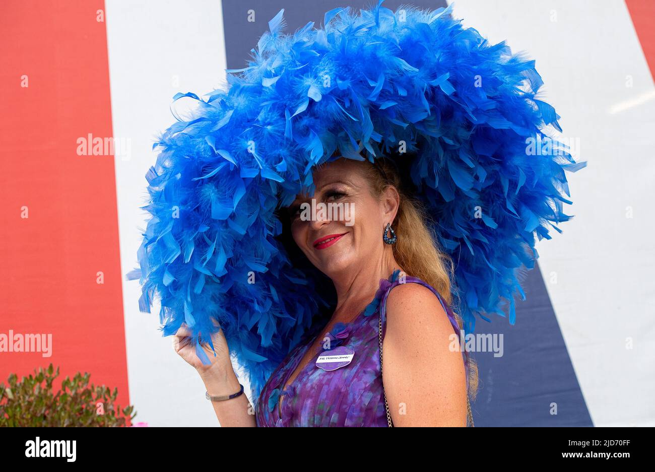 Ascot, Berkshire, UK. 18th June, 2022. Milliner Viv Jenner wears a large blue feathered hat. Racegoers arriving at Royal Ascot were looking very glamourous for the final day of Royal Ascot. After a week of glorious sunshine there were a few spots of rain this morning so the umbrellas were in action for a while. Credit: Maureen McLean/Alamy Live News Stock Photo
