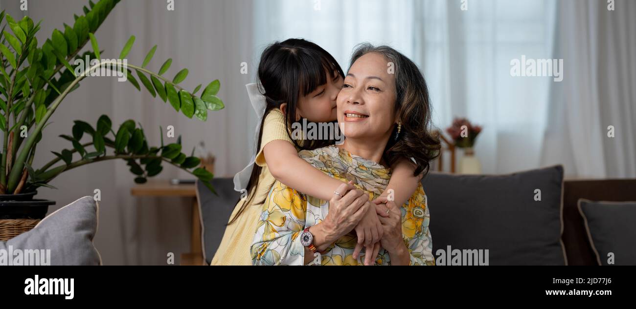 granddaughter kissing with love her mature woman grandmother preschooler at home on sofa Stock Photo