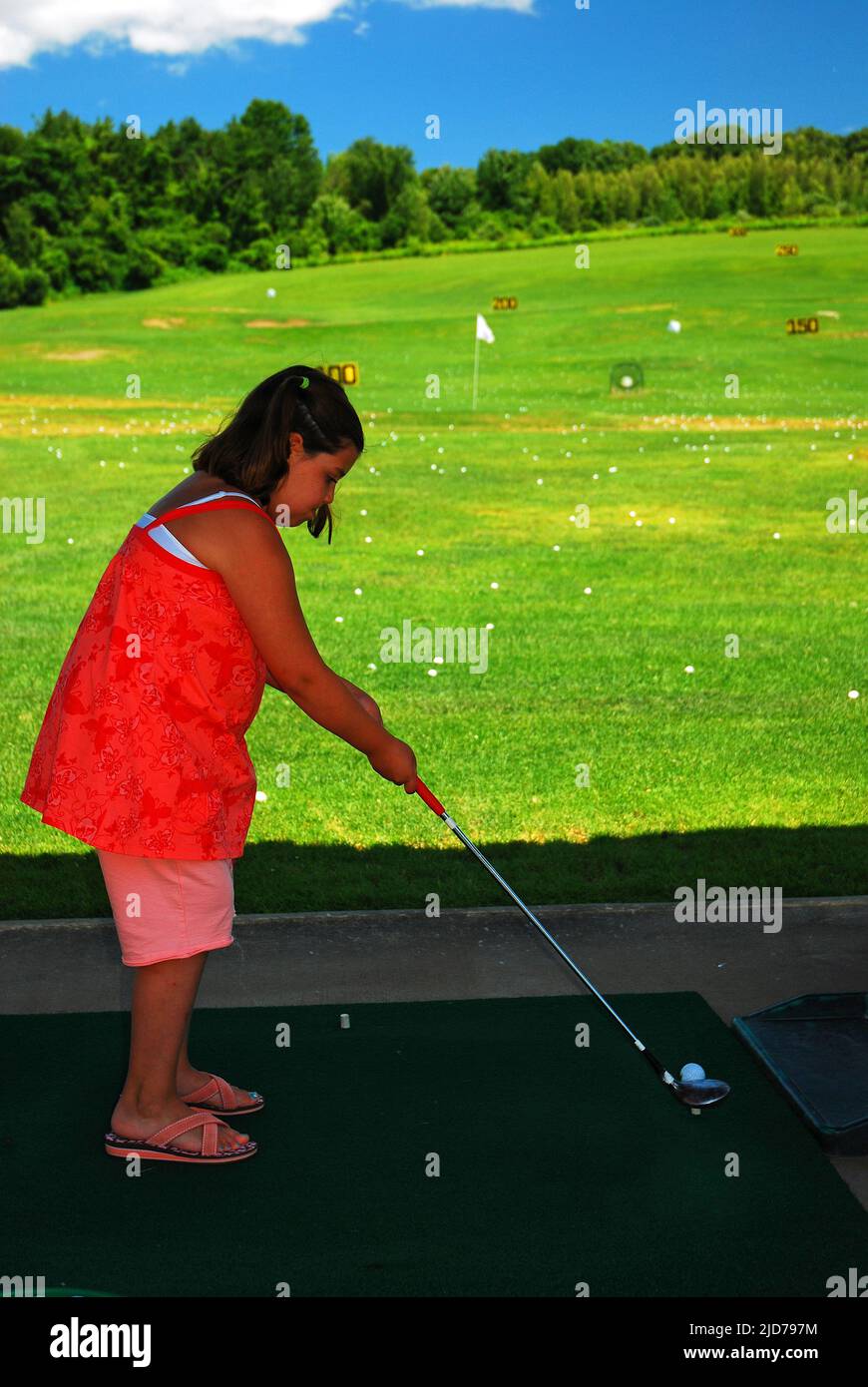 A young girl tees up at a golf driving range Stock Photo