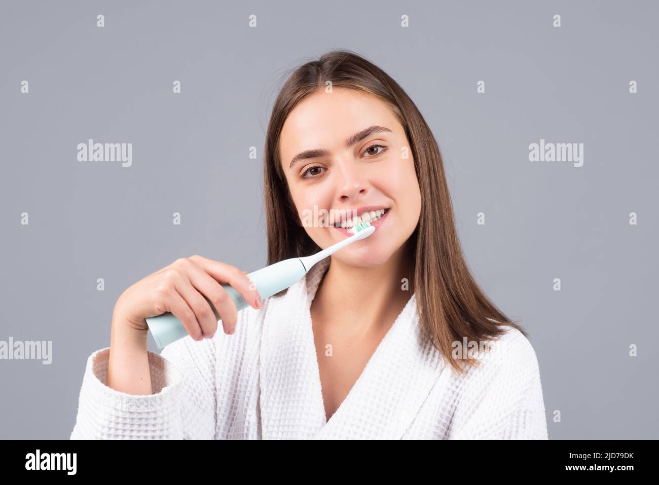 Smiling young woman brushing teeth using toothbrush with whitening