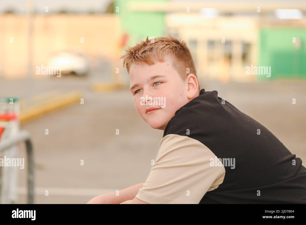 Relaxed preteen boy hanging out in urban car park. Blonde hair blue eyes. Stock Photo