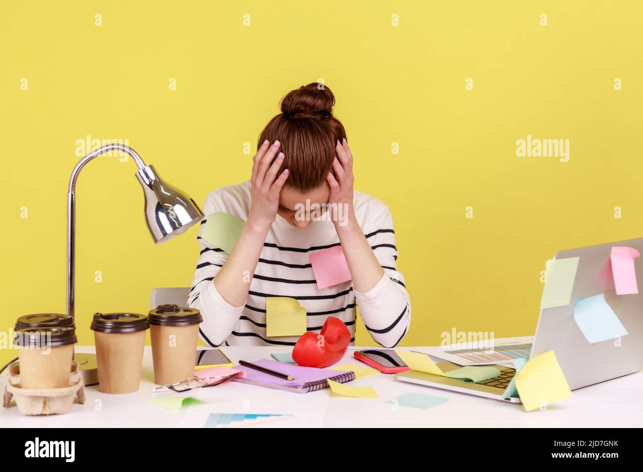 Tired exhausted overworked woman office worker covered with sticky notes, clasping head, thinking desperate, suffering headache. Indoor studio studio shot isolated on yellow background. Stock Photo