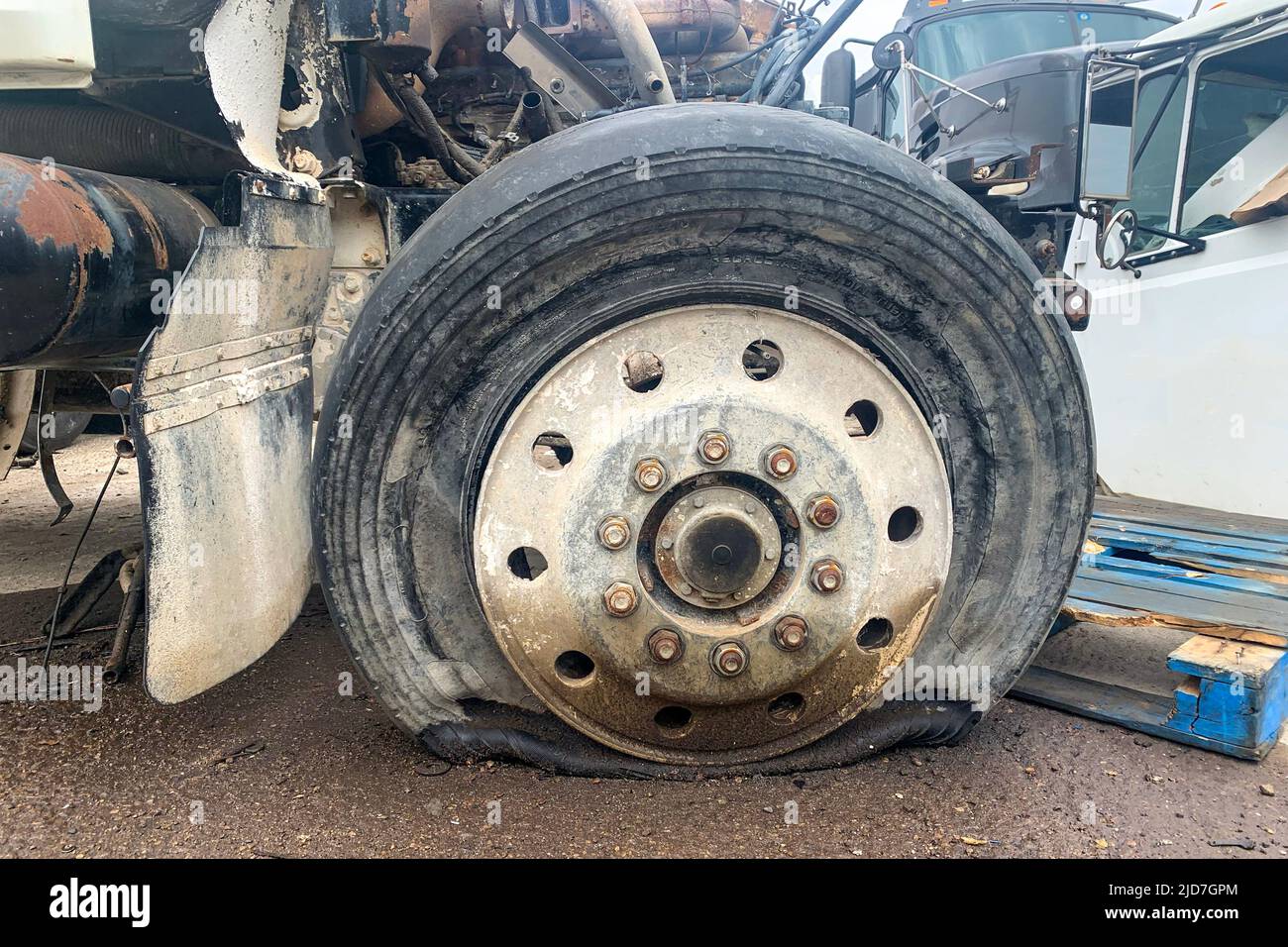 Closeup of wrecked truck wheel with a punctured or flat tire at a car junkyard after a traffic accident Stock Photo