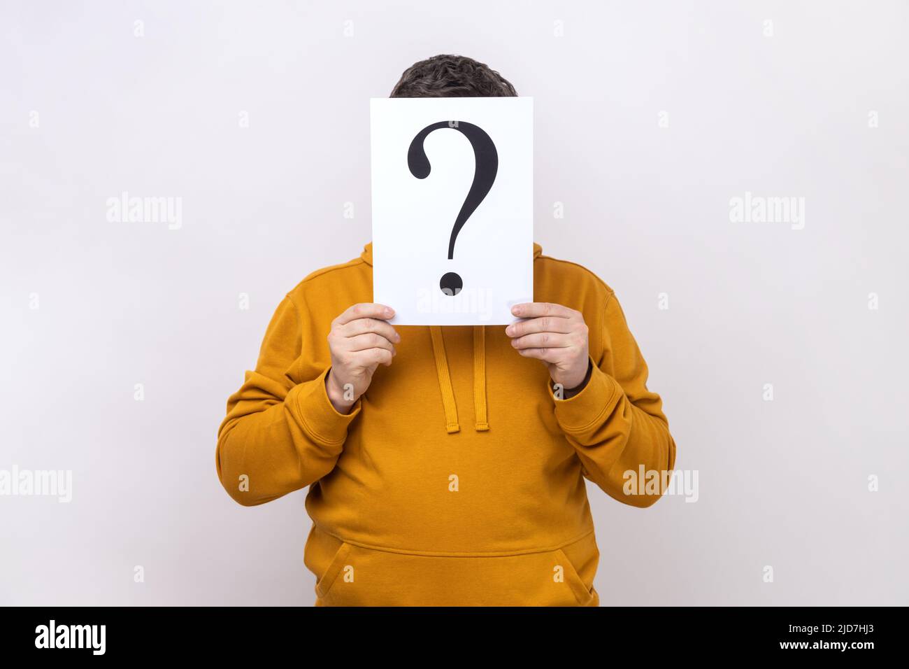 Portrait of anonymous unknown man covering his face with paper with question mark, finding right solution, wearing urban style hoodie. Indoor studio shot isolated on white background. Stock Photo