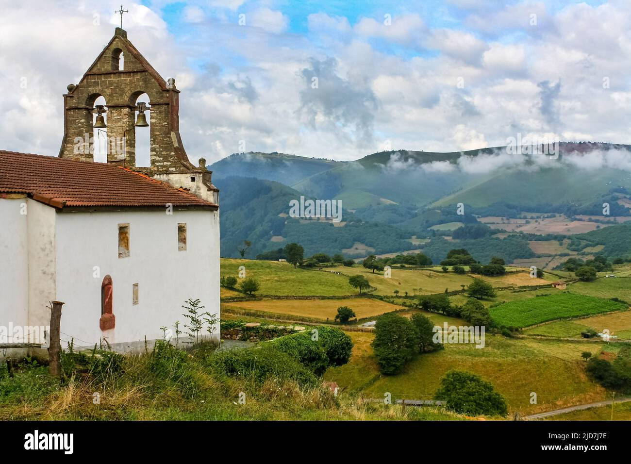 Ancient church with bell tower in the green field with high mountains in the background. Asturias Spain Europe. Stock Photo