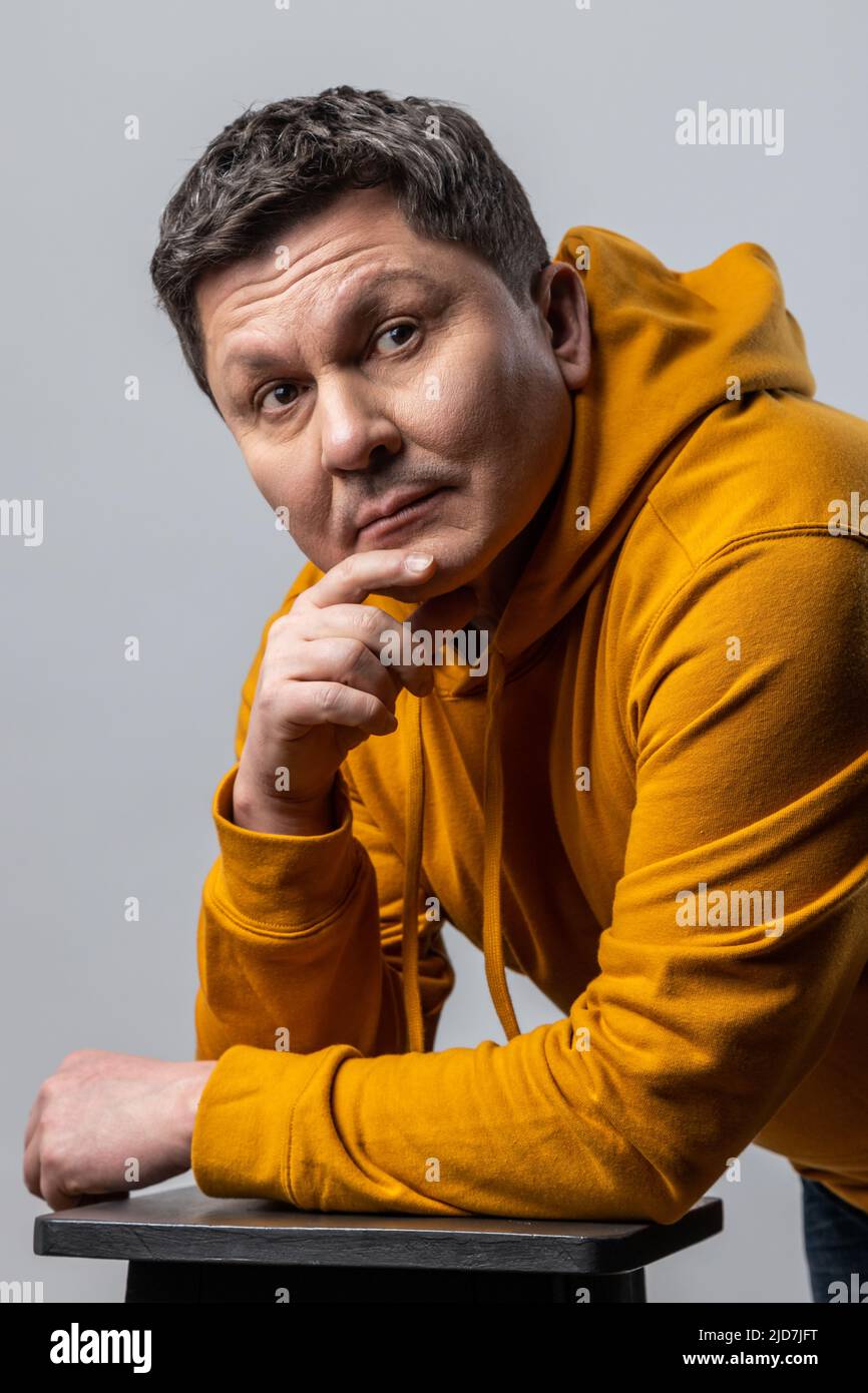 Portrait of pensive middel aged man, standing leaning on a chair with his hands, looking away, expressing thoughtfulness, wearing urban style hoodie. Indoor studio shot isolated on white background. Stock Photo