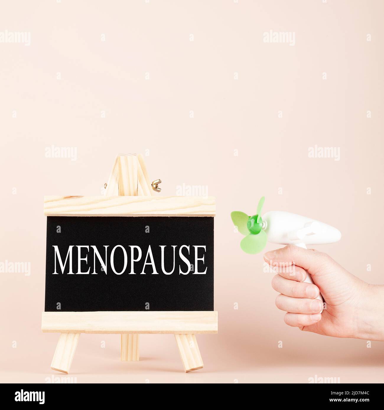 menopause word written on black board and hand holding fan on beige