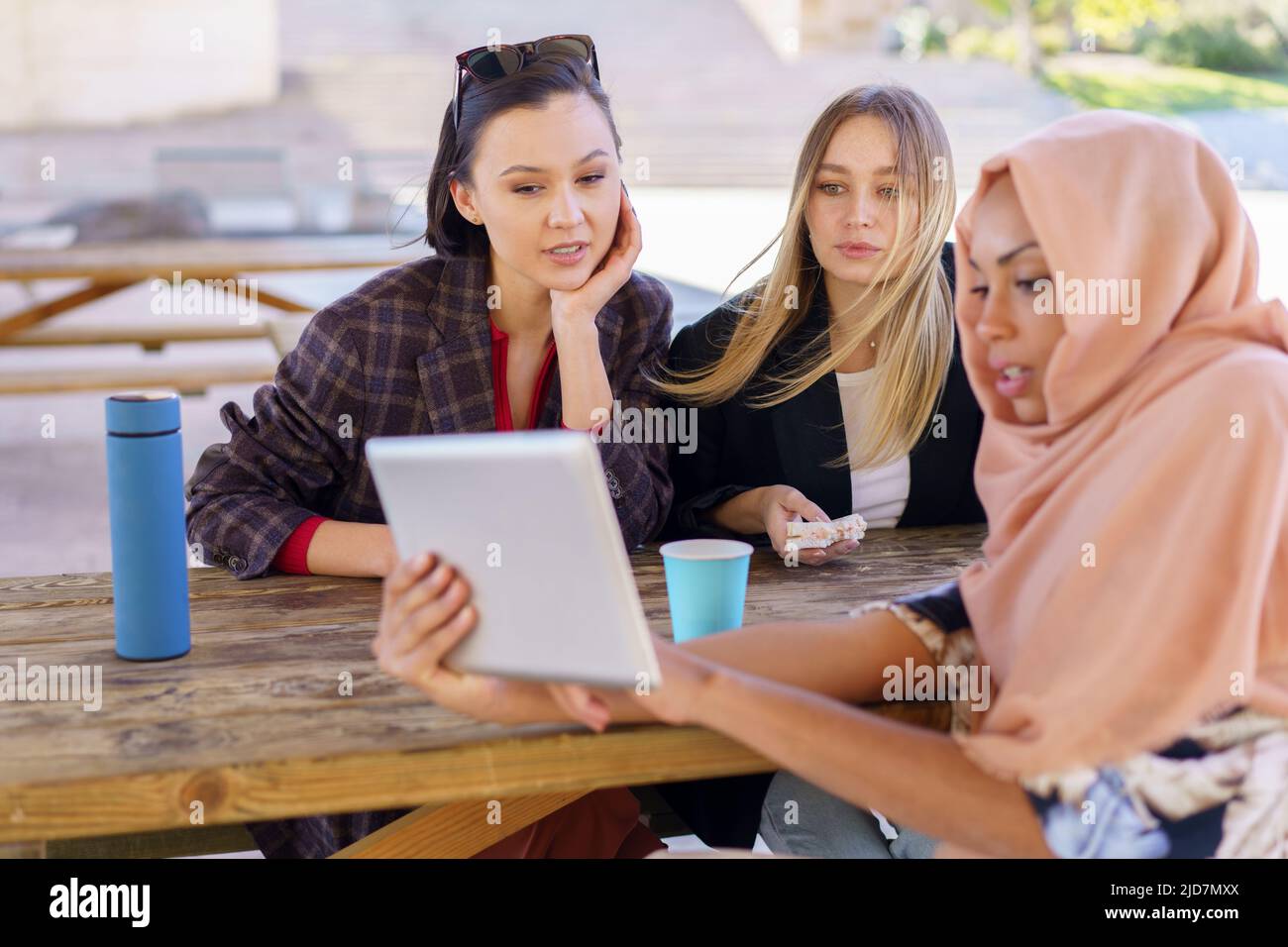 Cheerful diverse women sharing tablet during coffee break in cafe Stock Photo