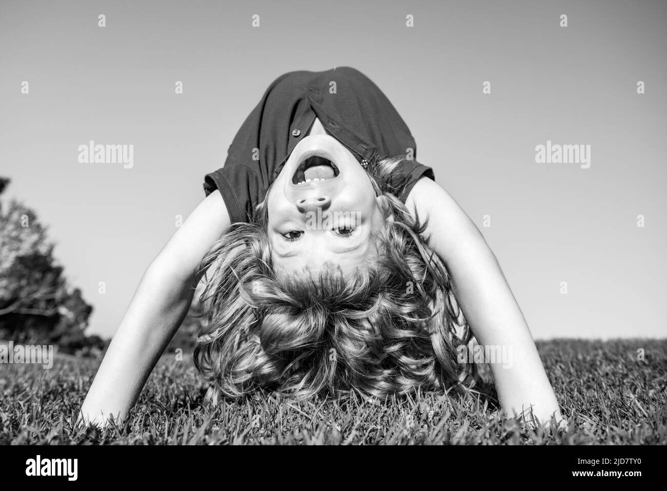 Portrait of a happy smiling child boy upside down on grass field. Laughing child. Expressive facial expressions. Active healthy outdoor sport. Fun Stock Photo