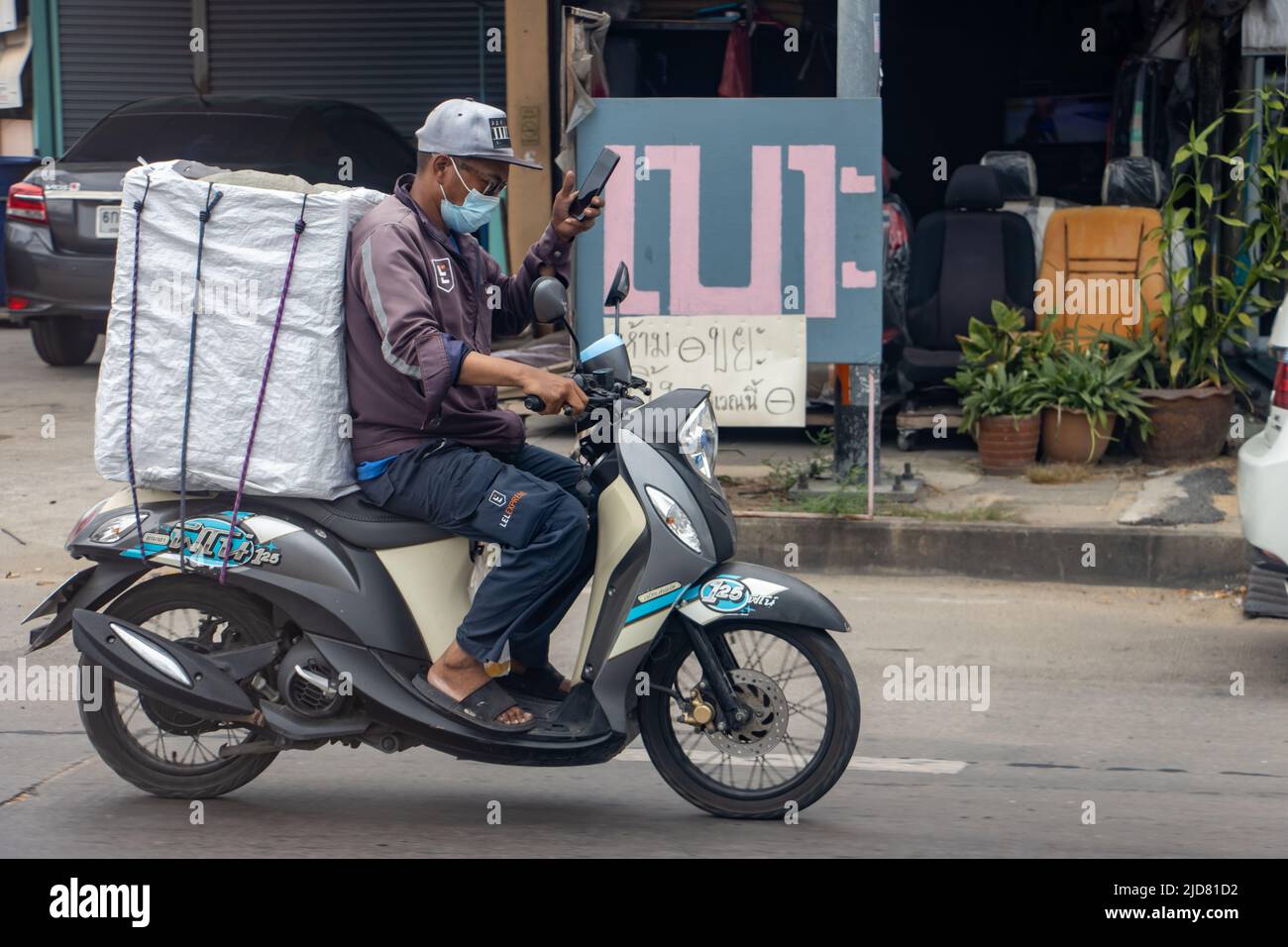 SAMUT PRAKAN, THAILAND, MAY 08 2022, A courier rides a motorcycle on the street and using his cell phone Stock Photo