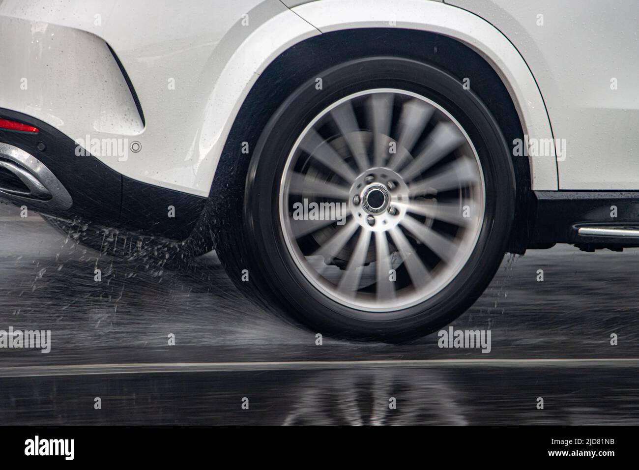 Detail of the rear wheel of a car driving in the rain on a wet road. Stock Photo