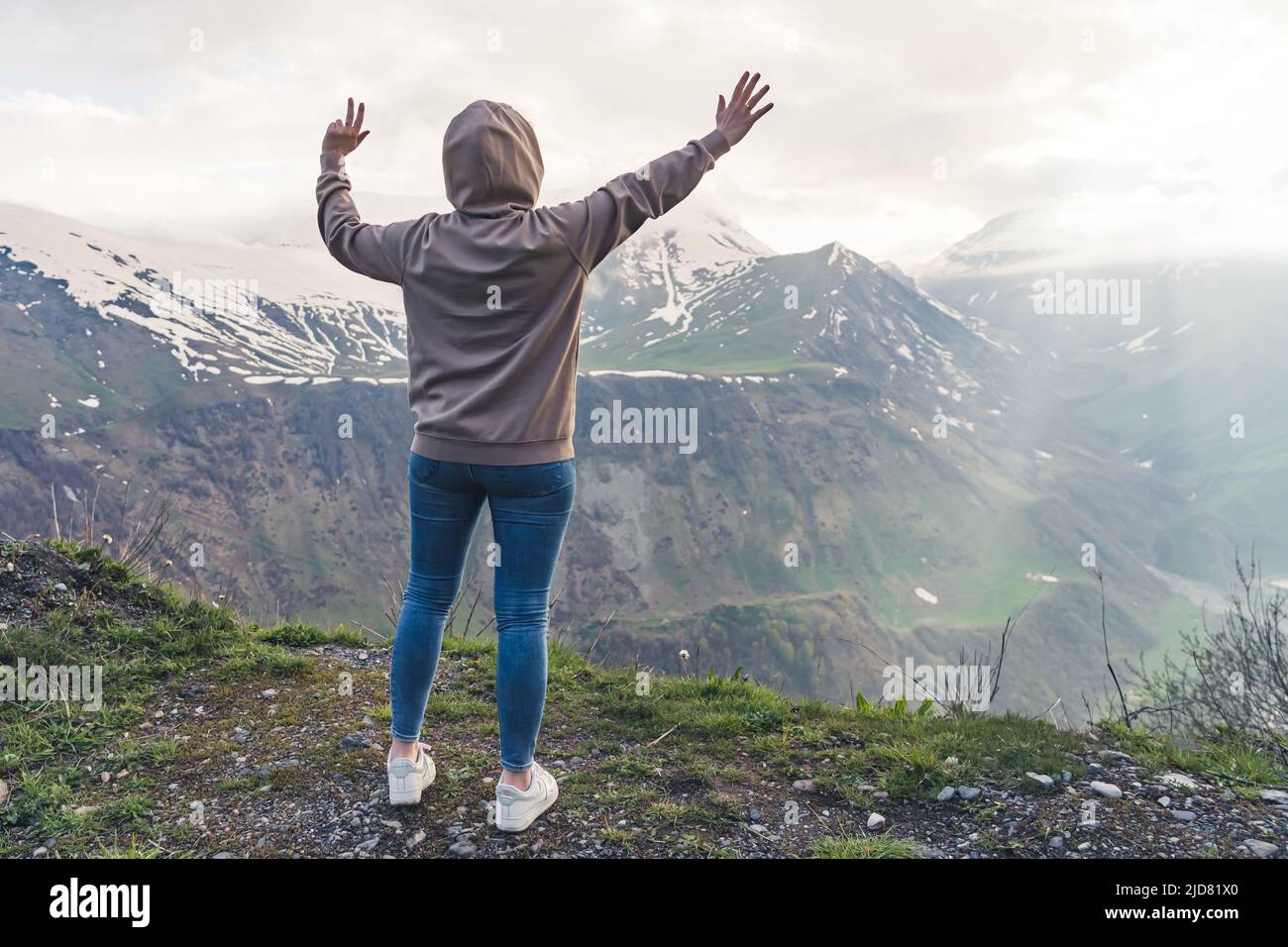 Back view of a woman dressed in casual clothes lifting her arms up watching a beautiful morning mountain landscape. High quality photo Stock Photo