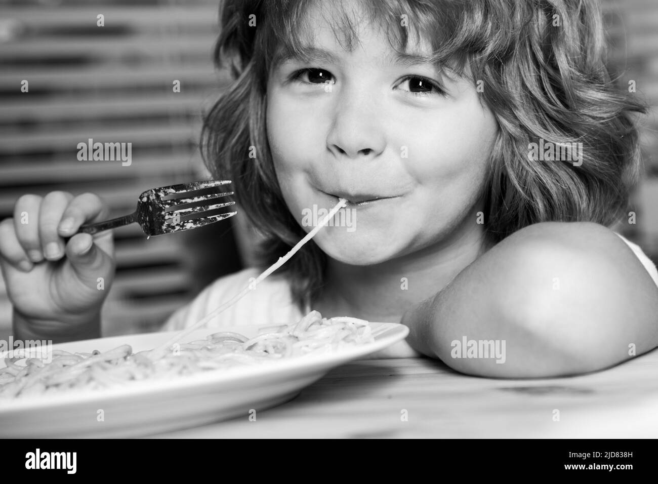 Caucasian smiling child eating pasta, spaghetti, portrait close up