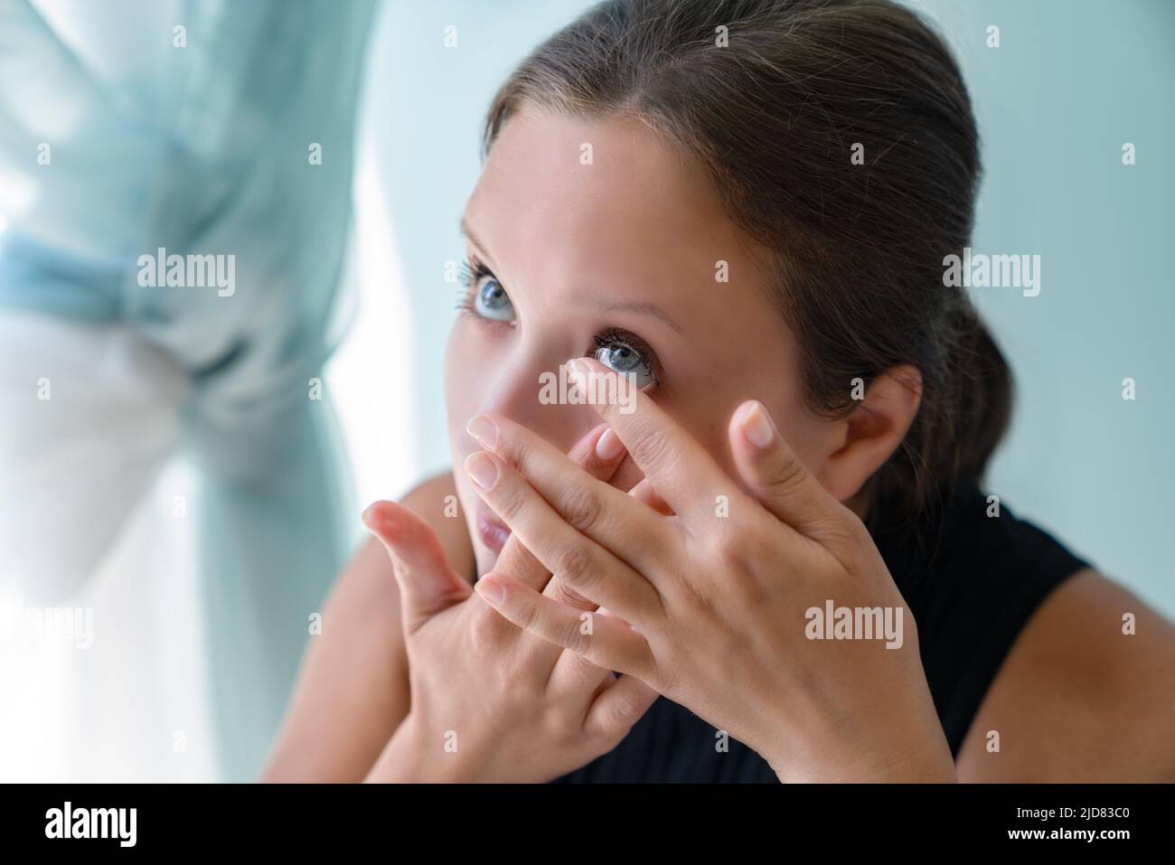 Young grl pulled back her lower eyelid and brought contact lens to her eye to put. Stock Photo