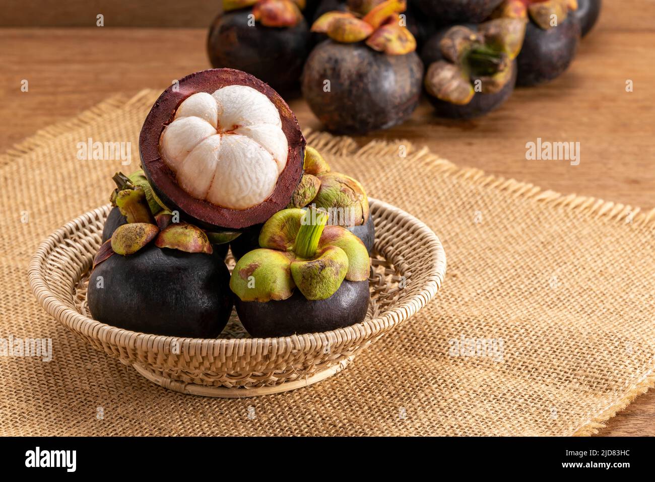 Pile of fresh mangosteen fruit in bamboo basket on sackcloth and in the background on wooden table. Stock Photo