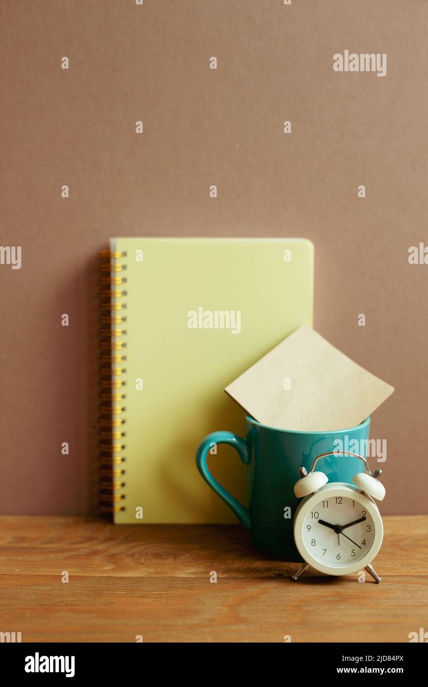 Notebook and mug cup and alarm clock on wooden desk. brown wall background. workspace Stock Photo