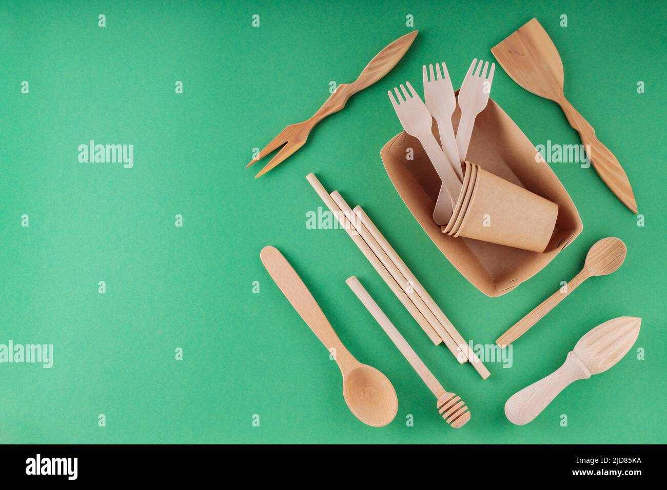 Paper biodegradable tableware and wooden cutlery on a green background. Eco-friendly kitchen utensils, bamboo forks, cardboard containers and cups. Su Stock Photo