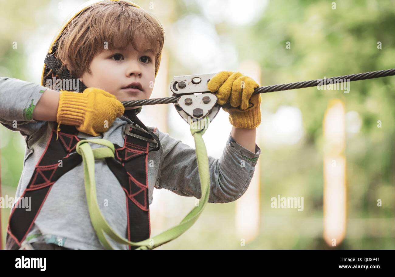 Children summer activities. Portrait of a beautiful kid on a rope park among trees. Every childhood matters. Active children. Roping park. Stock Photo