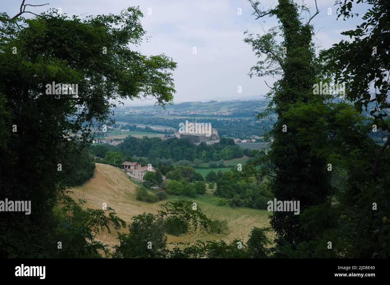 View to valley and castle called Castello di Torrechiara through lush foliage in Parma province, Italy. Typical Italian landscape with harvested field Stock Photo