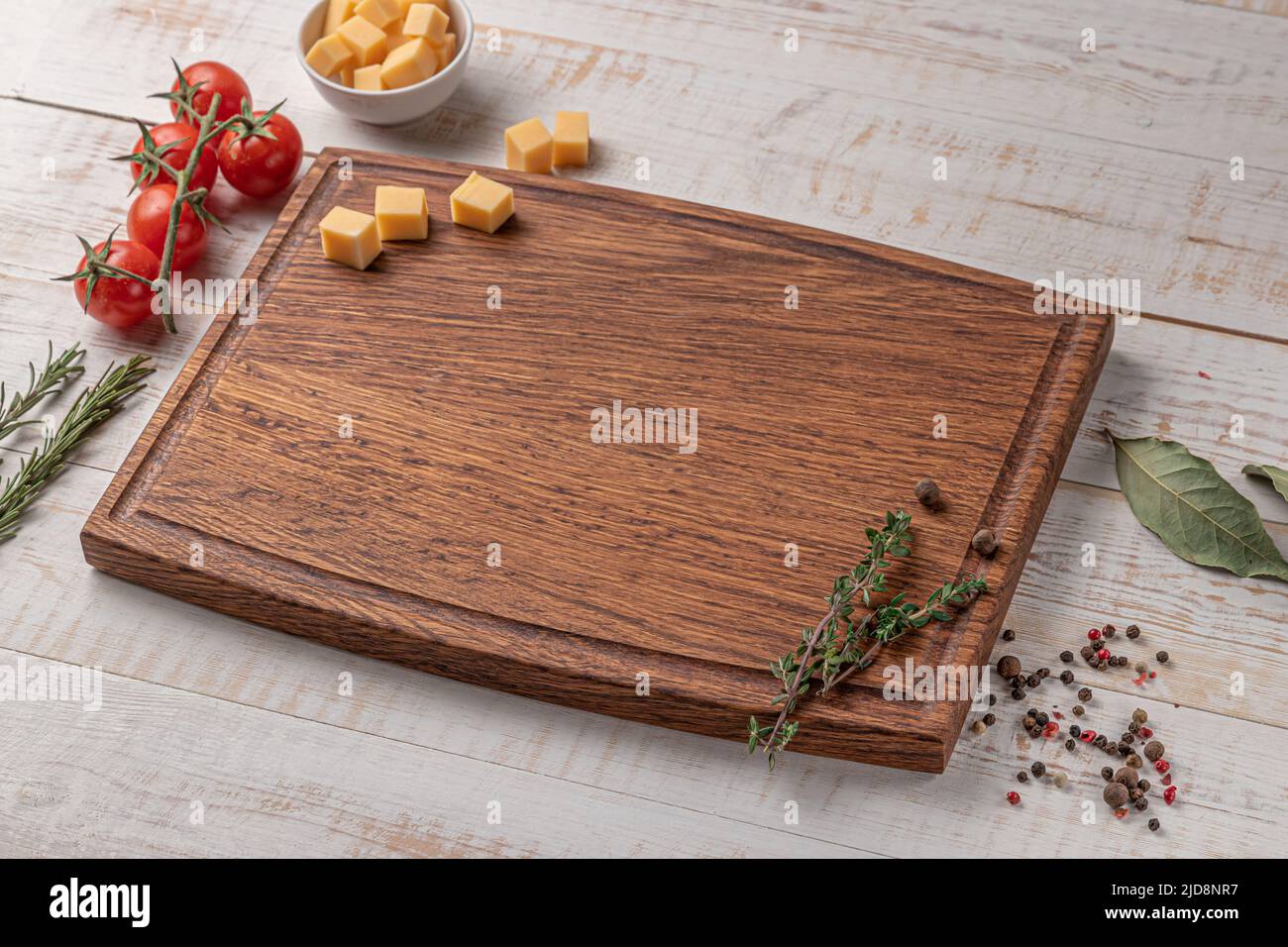 square wooden cutting board with edging. cherry tomatoes, slices of cheese and spices on a white background. mockup with copy space for text, side vie Stock Photo