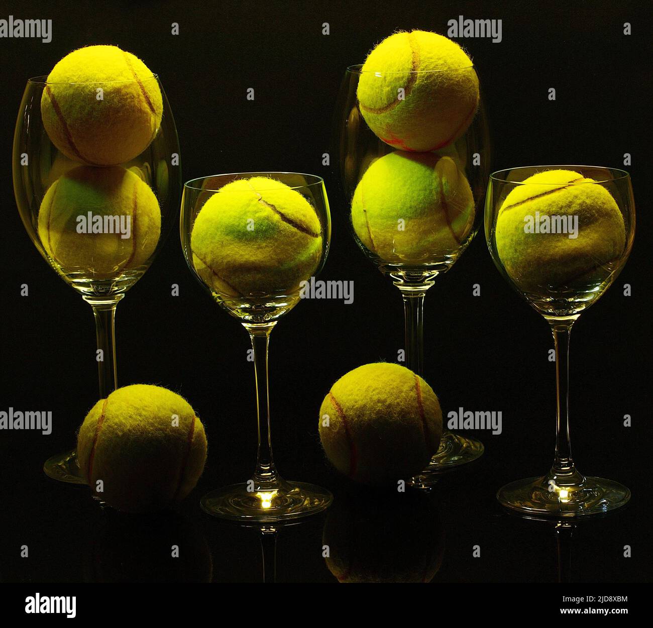 Tennis ball and wine glass in a black background, illuminated from above in a long exposure shot. Stock Photo