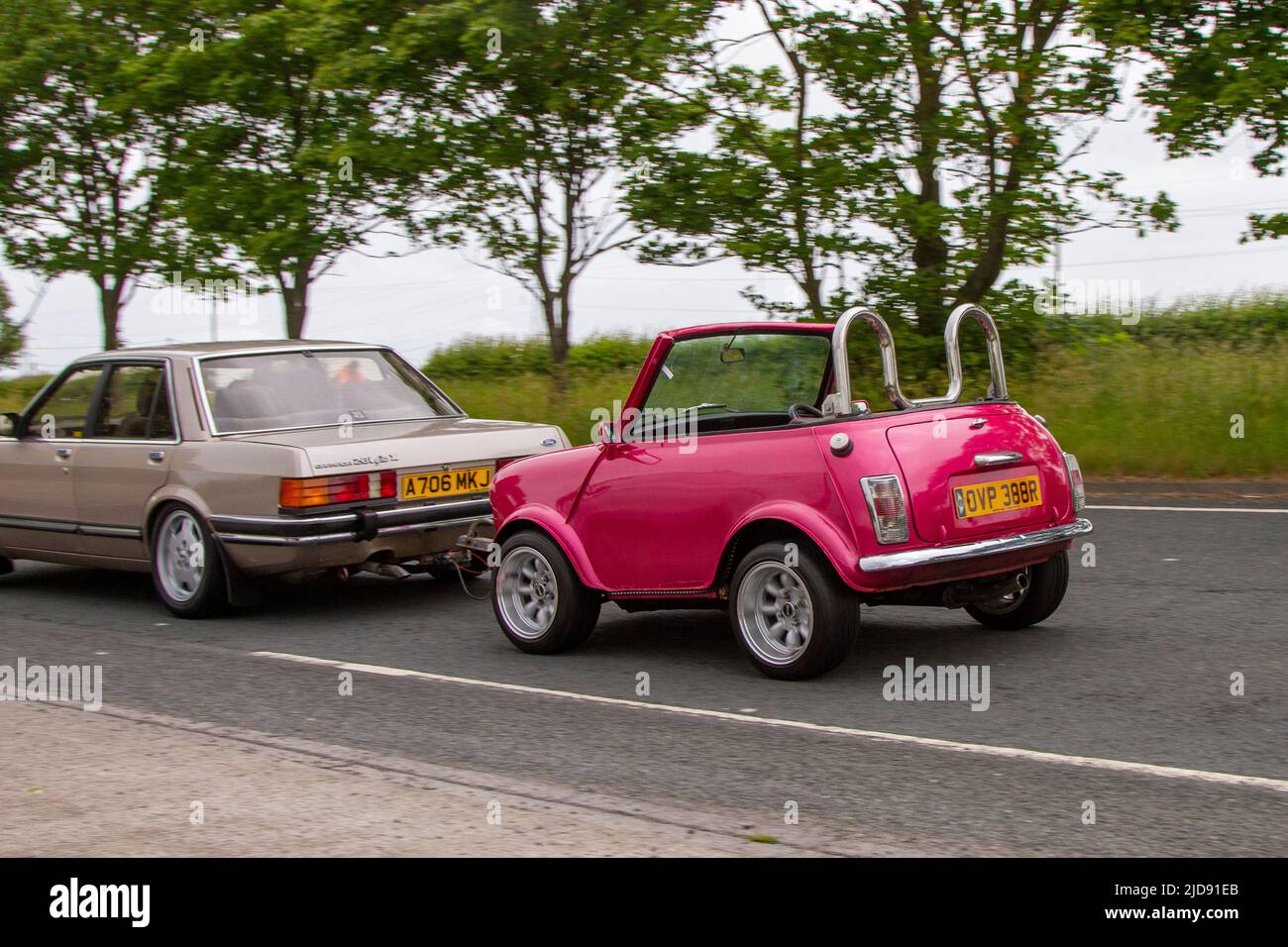 1977 70s seventies pink Leyland Mini 1000 cars 998cc customised shortened vehicle being towed by 1983 80s Ford Granada;  classic, modern classic, supercars and specialist vehicles en-route to Lytham St Annes, Lancashire, UK Stock Photo