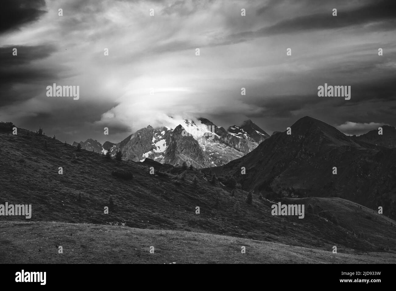 Sunlight on Marmolada mountain group. Moving clouds. Dramatic sky. The Dolomites. Italian Alps. Europe. Black white landscape. Stock Photo