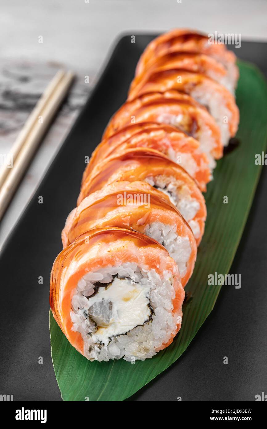 set of maki rolls with smoked eel and green bamboo leaf in a black ceramic plate with chopstick on a bright white textured marble background, side vie Stock Photo
