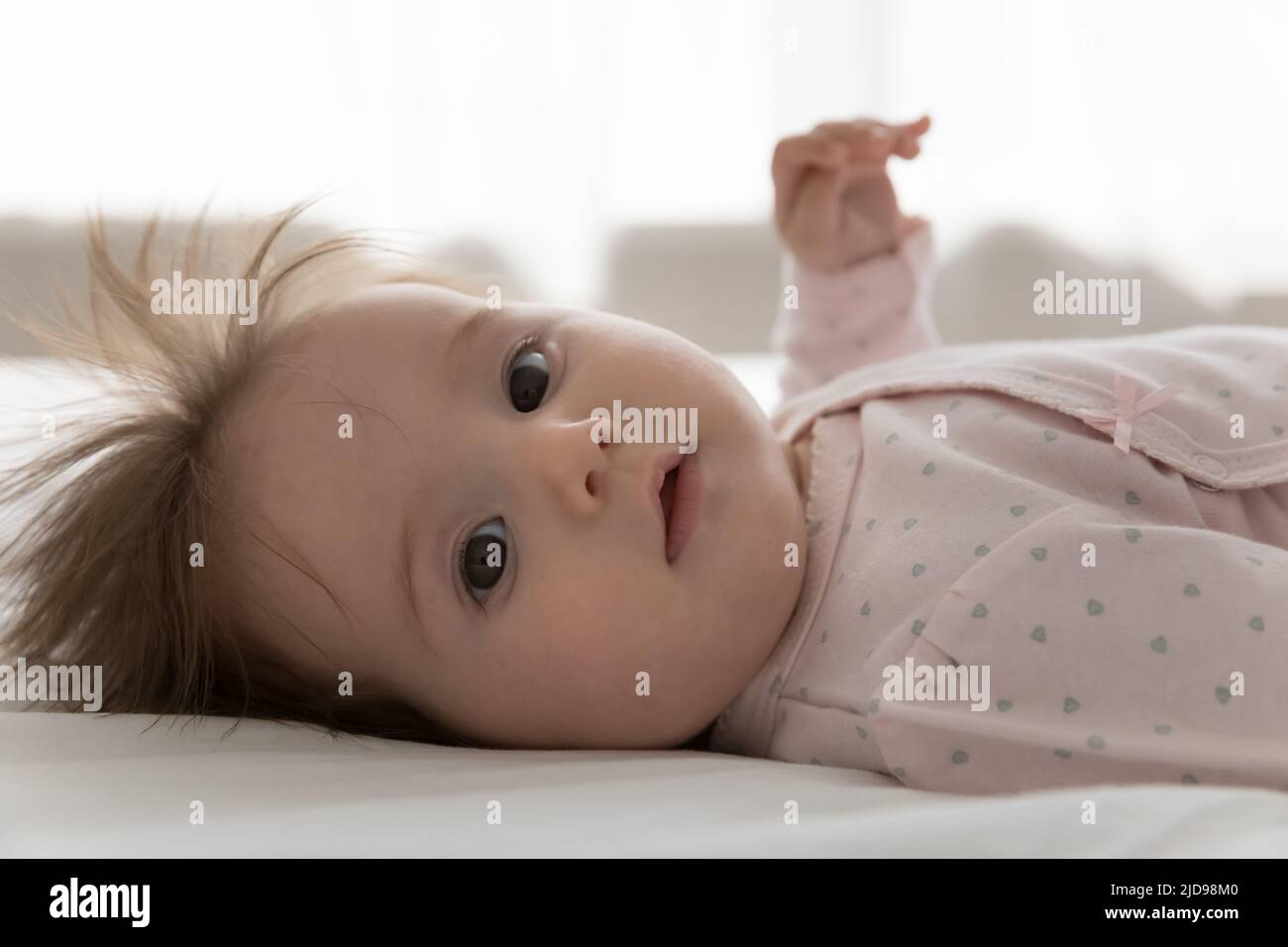 Cute infant in bodysuit lying on bed looking at camera Stock Photo