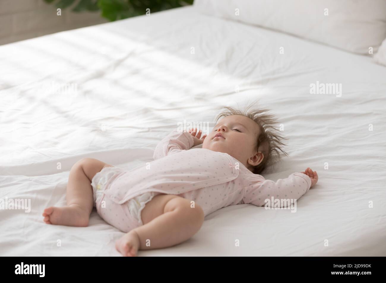Close up shot peaceful babygirl in bodysuit sleeping on bed Stock Photo