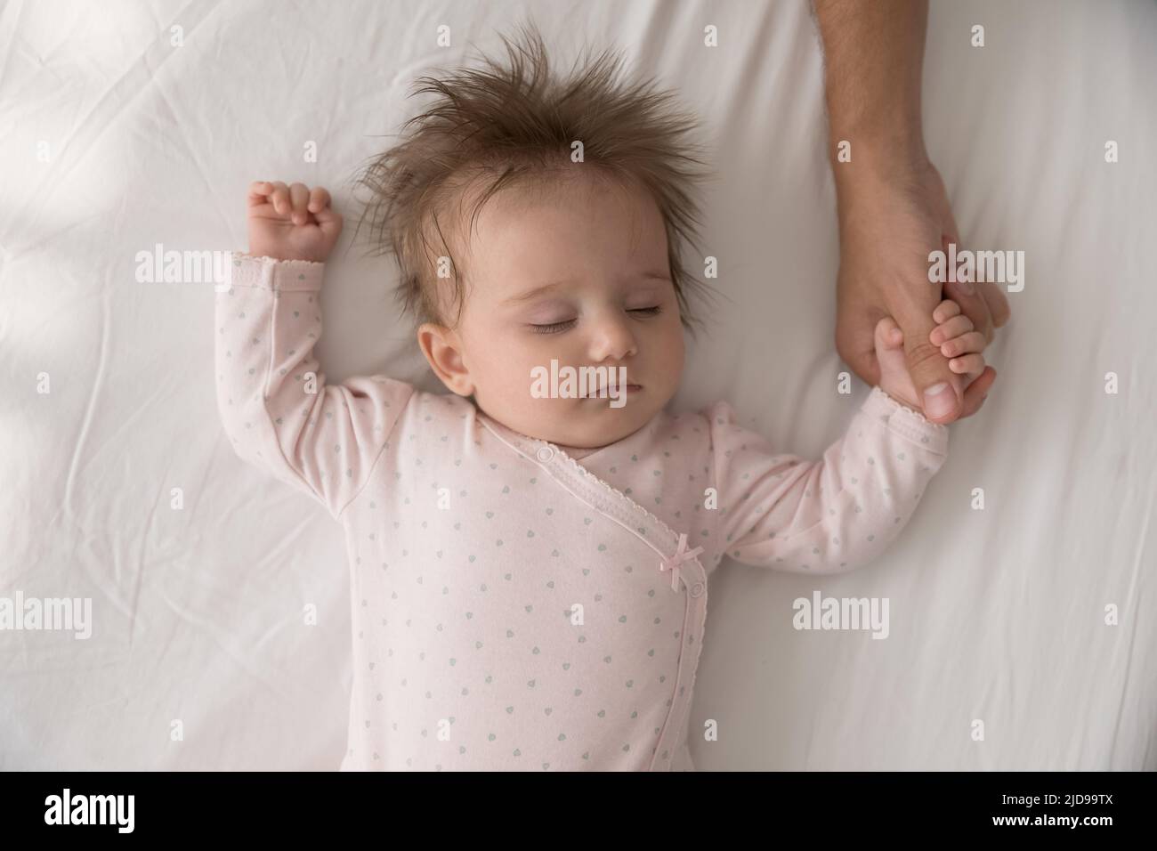 Serene babygirl sleeping on bed holding tightly loving daddy thumb Stock Photo