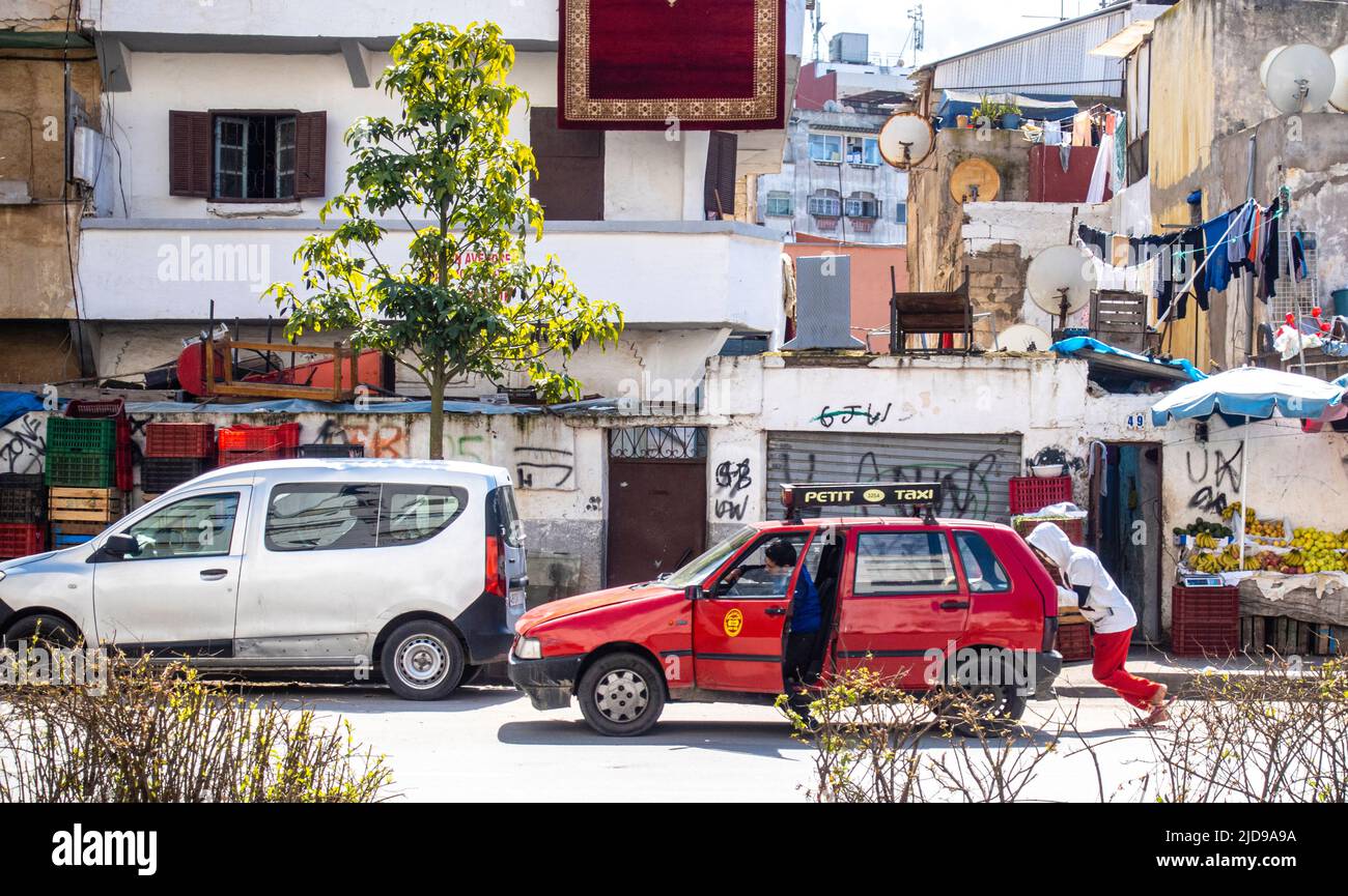 A man pushing a red taxi cab helping it move on  the road in the dense poor district of Bourgogne, Casablanca, Morocco Stock Photo