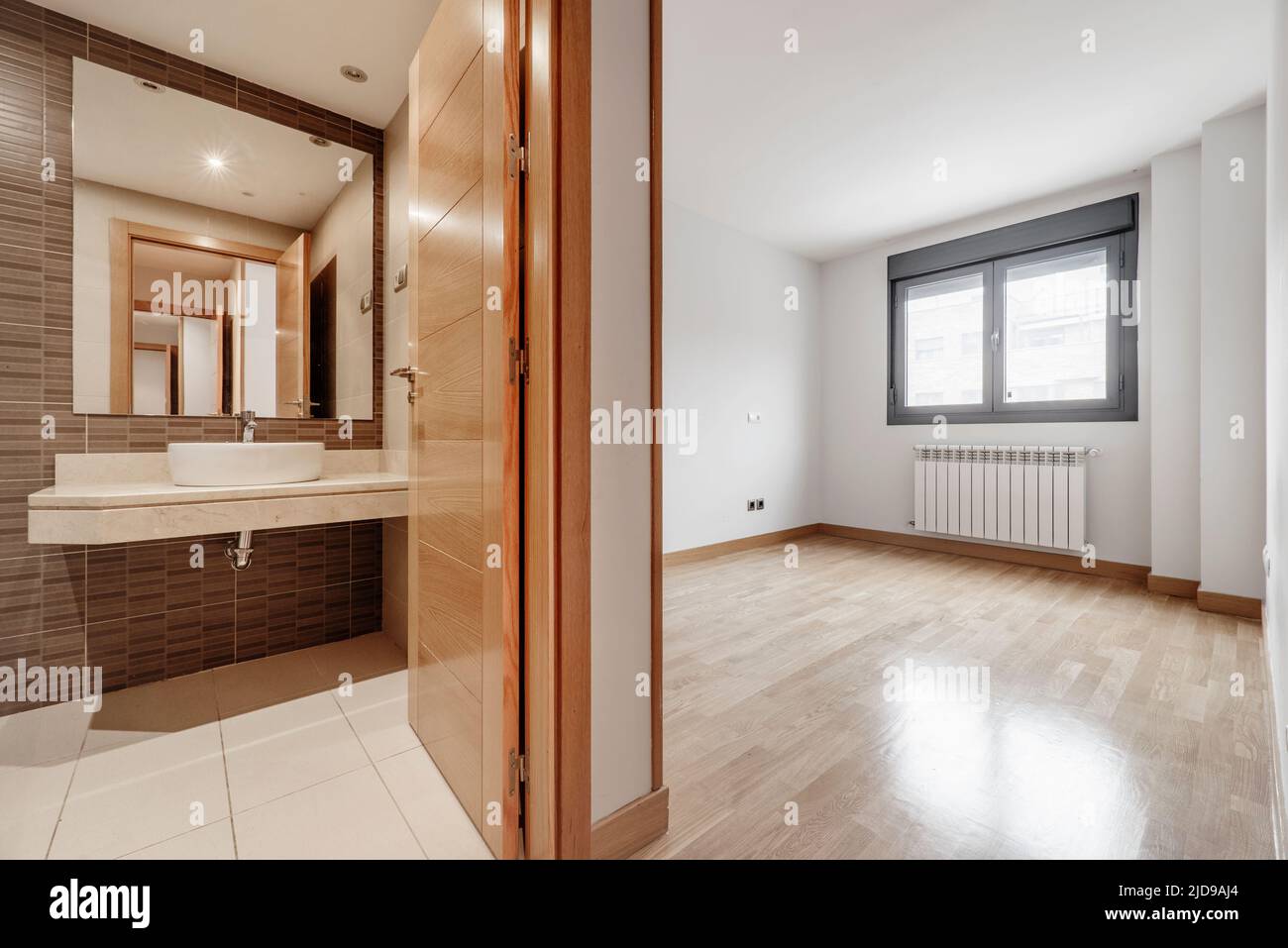 Empty room with aluminum window with views, French oak parquet flooring, en-suite bathroom with marble top and large white aluminum radiator Stock Photo