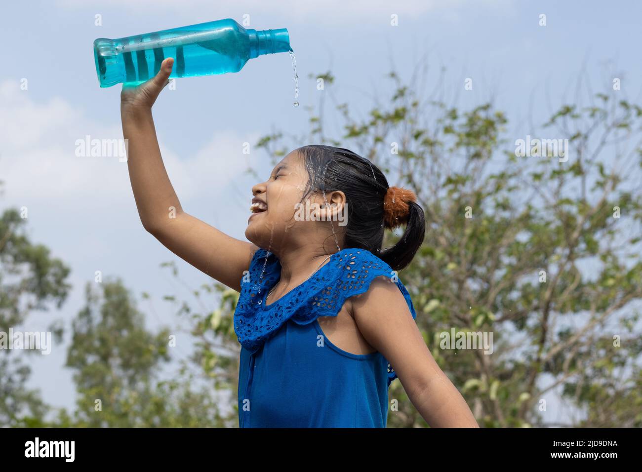 An Indian girl pouring water on head from a blue plastic bottle under