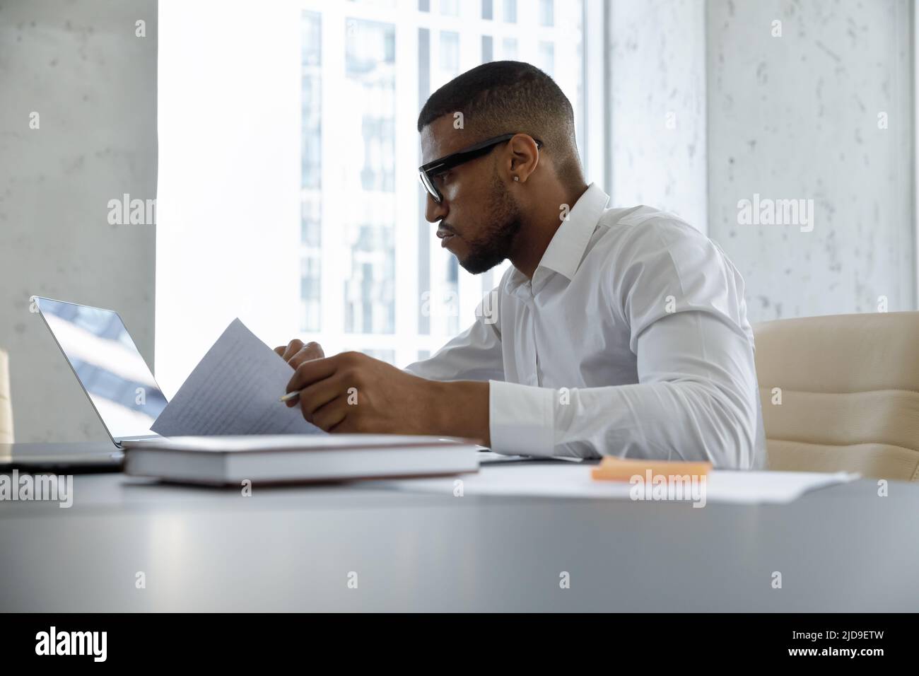 Serious African businessman working with documents using laptop looking focused Stock Photo