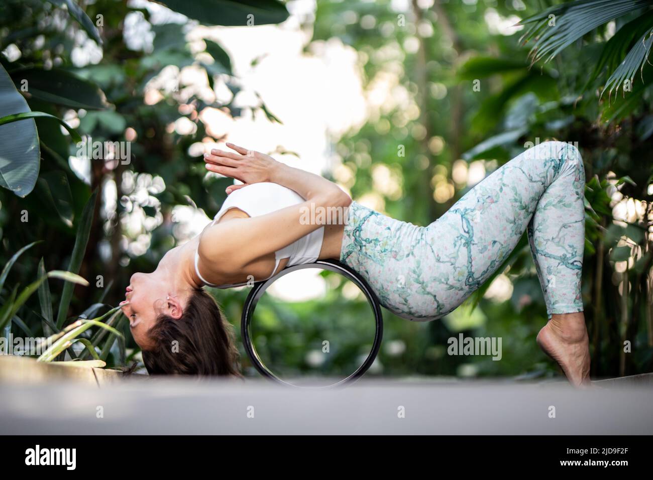 Female meditating and practicing yoga in tropical rainforest. Beautiful young woman practicing yoga outdoor with tropical forest in background. Stock Photo
