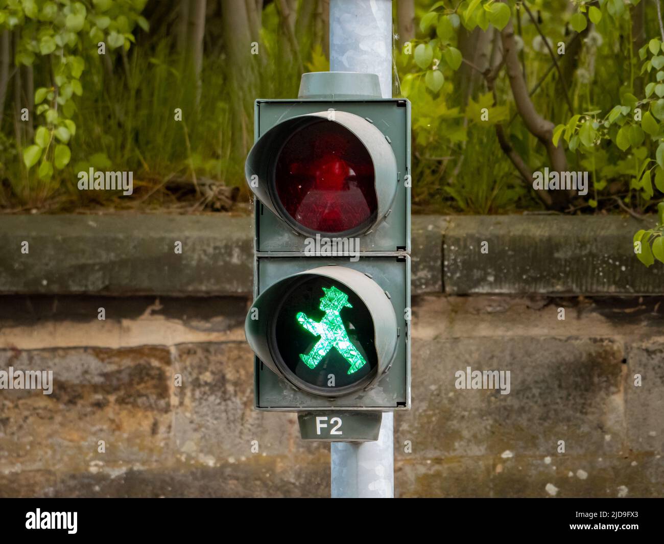 Traffic light for pedestrians showing a go symbol for crossing the street. A green illuminated walking figure is the signal for starting. Stock Photo