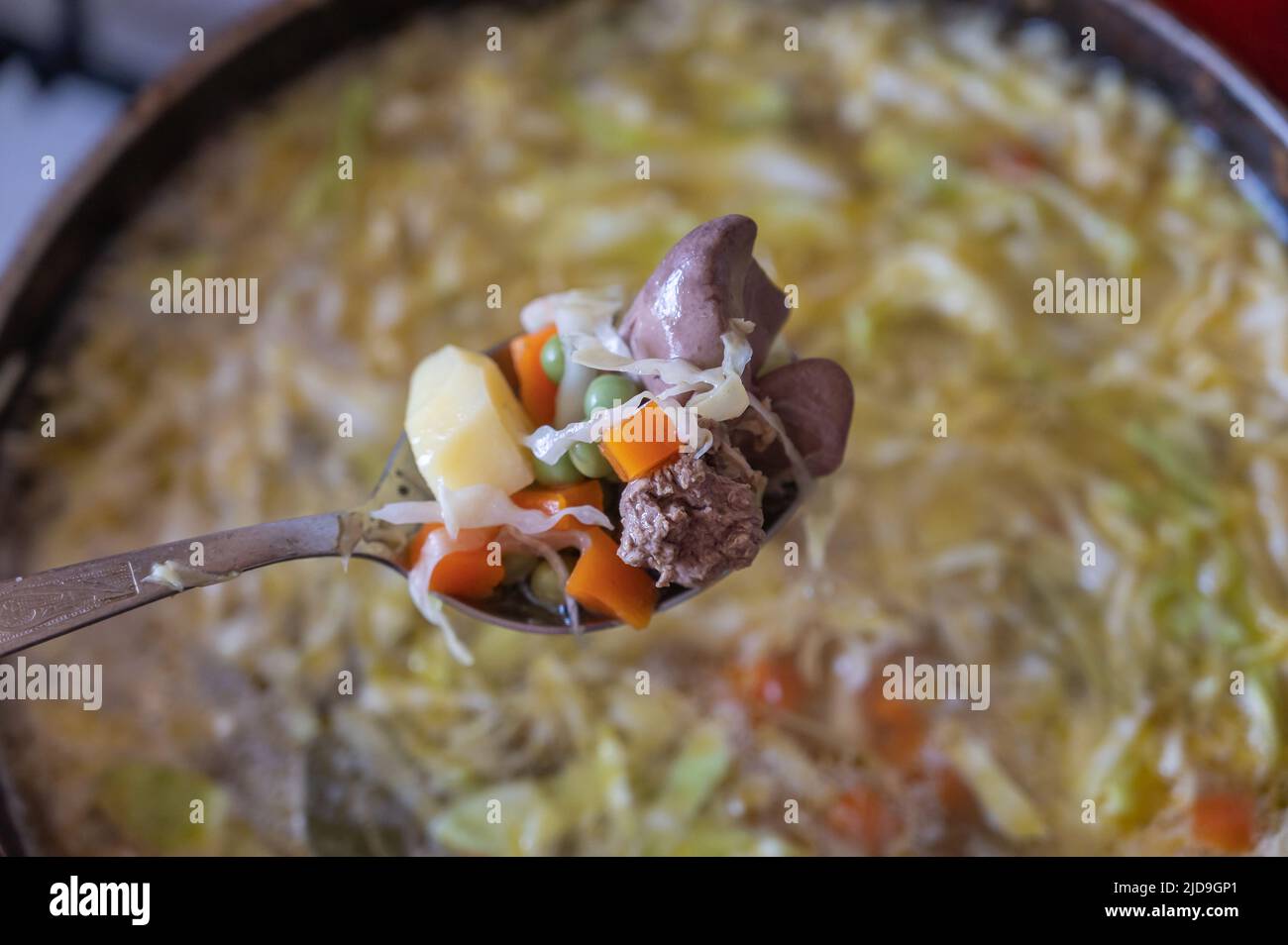 A spoon full of food. A delicious soup of cabbage, potatoes, onions, carrots, green peas, chicken liver, salt and spices. A close-up view. Selective f Stock Photo