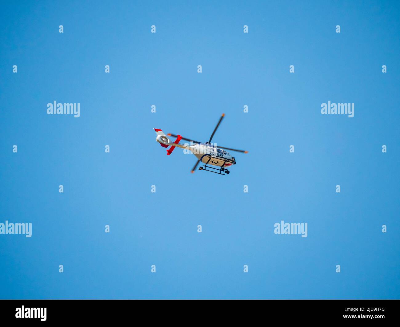 Police helicopter high up in the sky. German chopper from the police in saxony. The sky is blue and clear. People in the vehicle are observing. Stock Photo