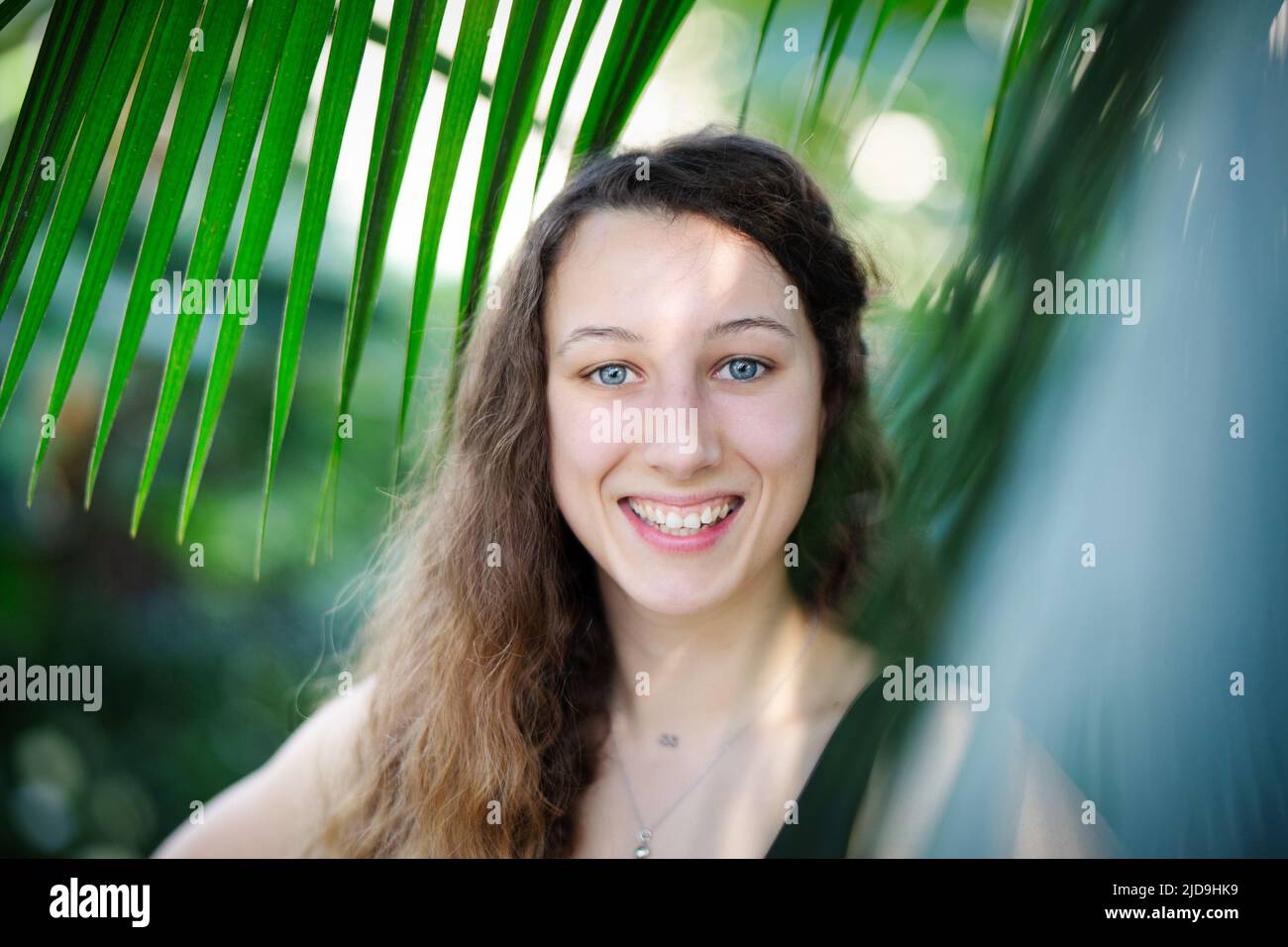 Young beautiful natural cheerful woman with healthy face and skin in exotic greenery. Closeup fresh face of attractive girl. Summer model. Natural Stock Photo