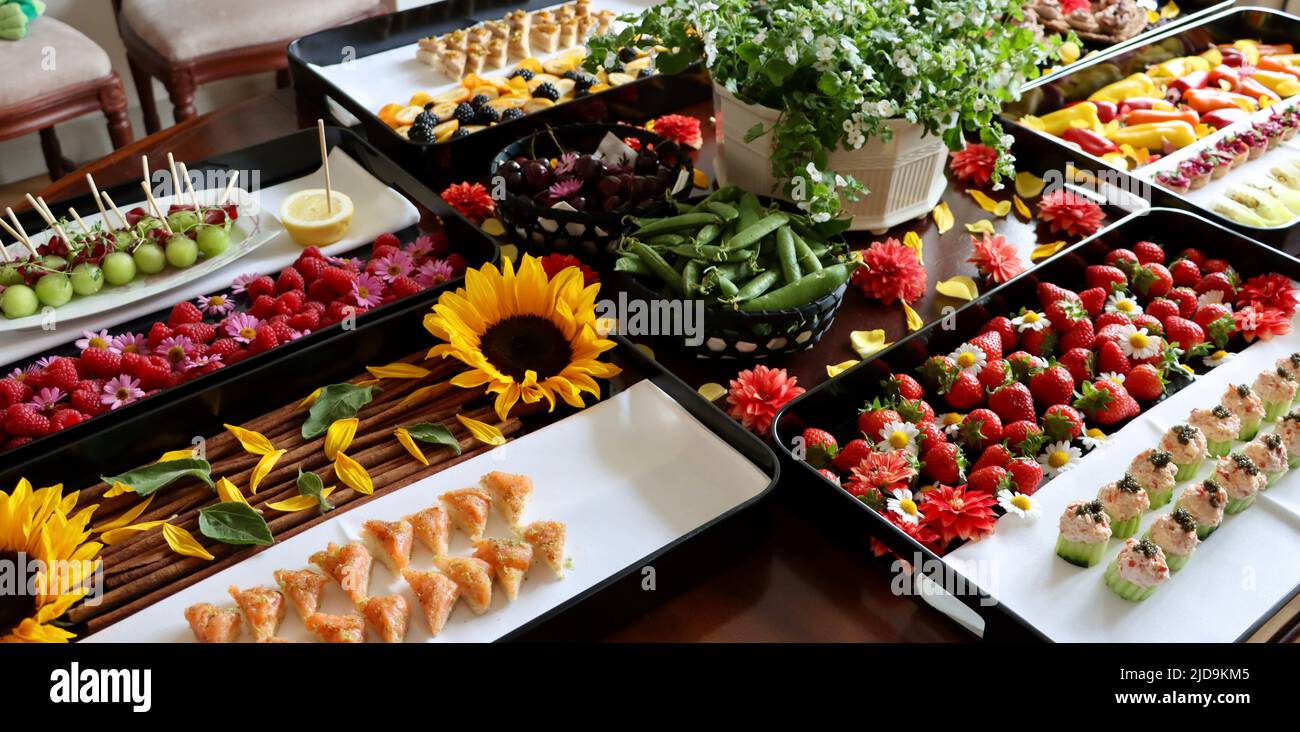 Selection of hors d'oeuvre on black trays decorated with flowers and berries. Stock Photo
