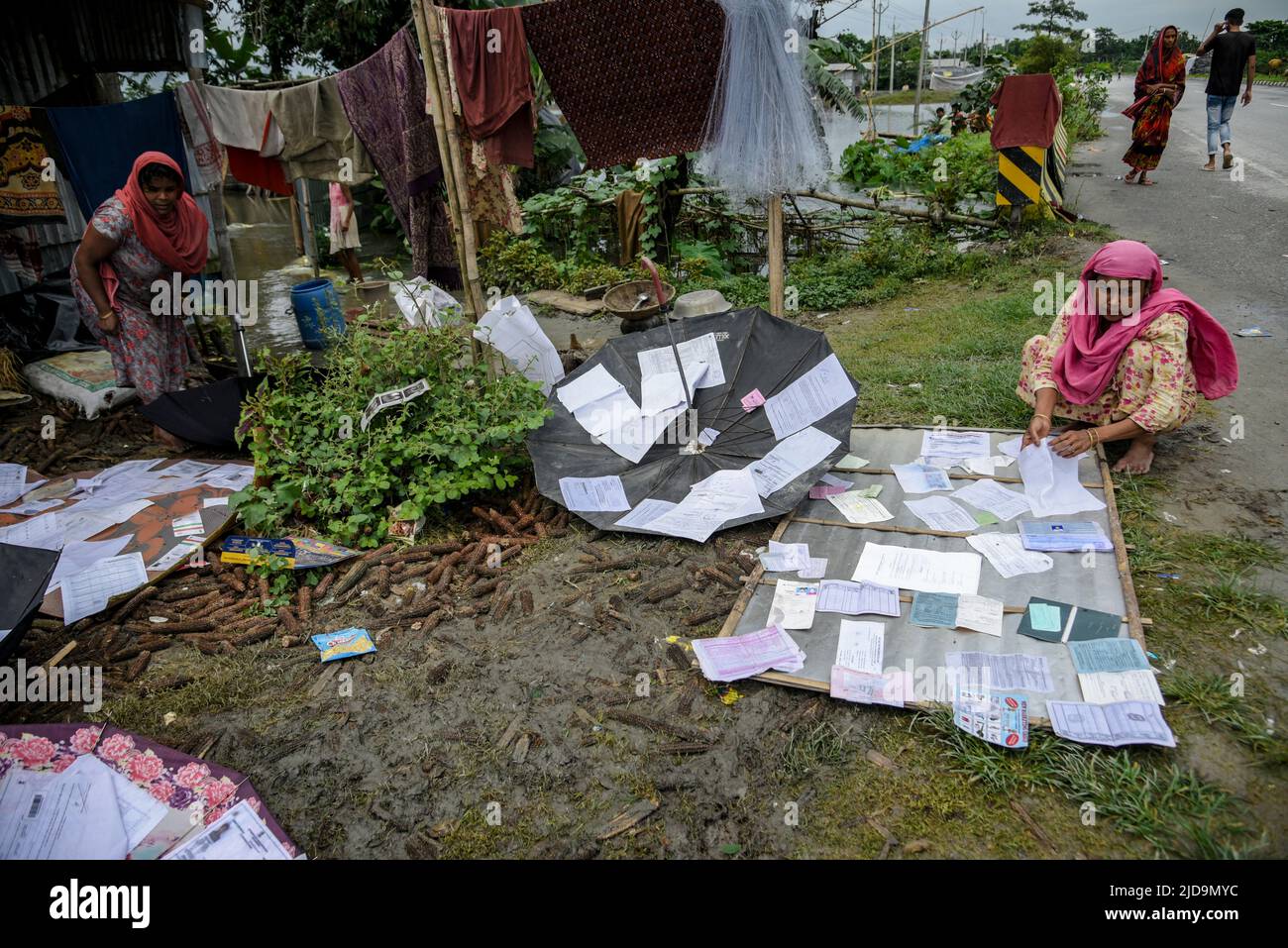 Women dry documents near a highway after their house submerged in flood water, at a village on June 17, 2022 in Barpeta, India. Assam flood situation deteriorates due to heavy rain, over a million people affected. Stock Photo