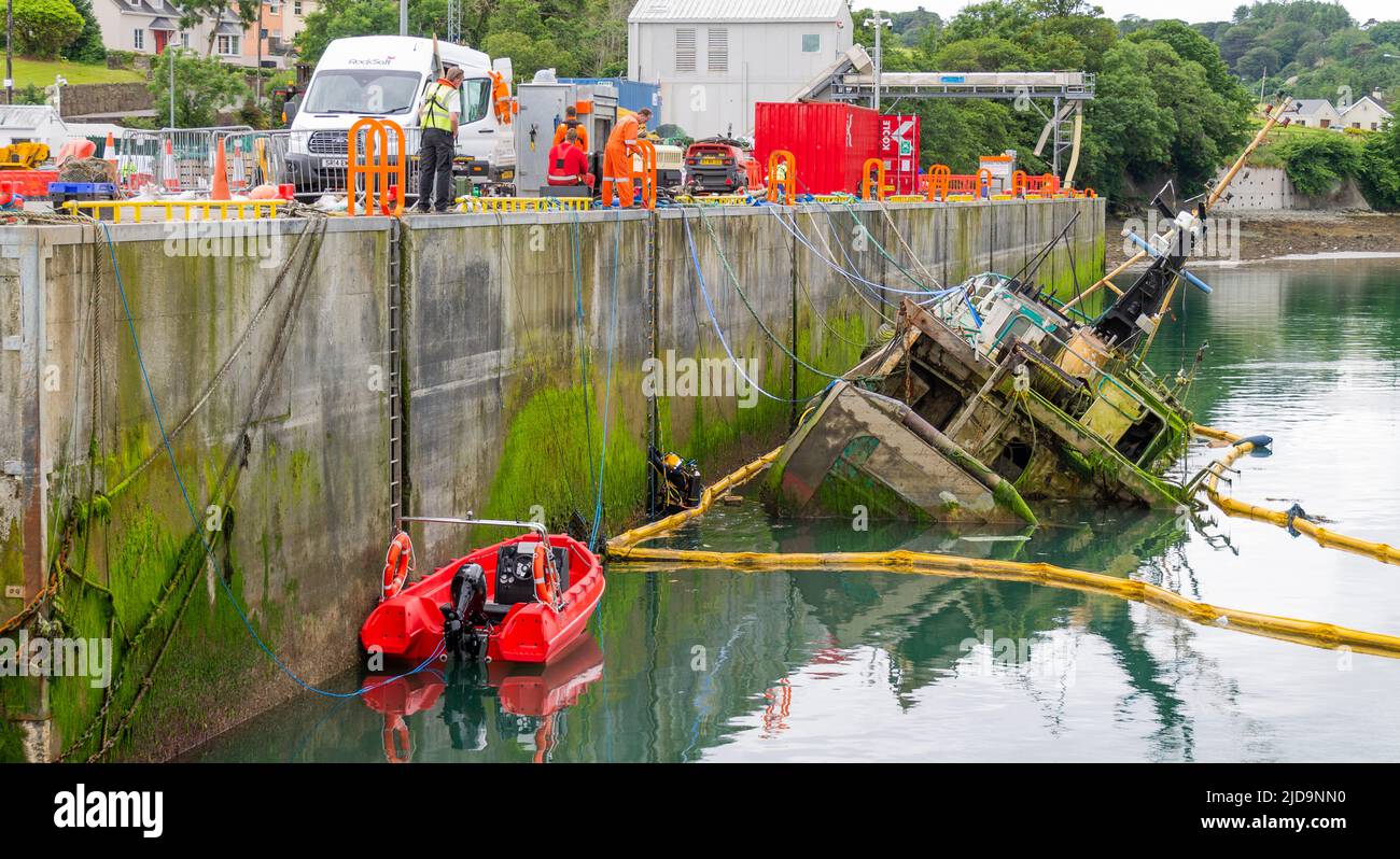 Salvage diver entering the water next to a partially sunken ship wreck Stock Photo